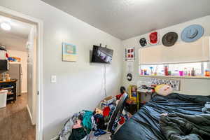 Bedroom featuring stainless steel fridge, wood-type flooring, and a textured ceiling