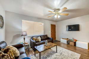 Living room with hardwood / wood-style floors, ceiling fan, and a textured ceiling