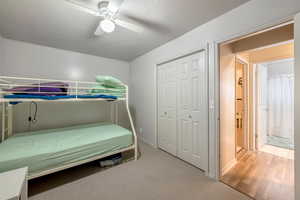 Carpeted bedroom with ceiling fan, a textured ceiling, and a closet