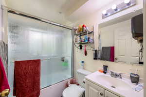 Full bathroom with vanity, bath / shower combo with glass door, and toilet