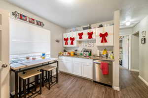 Kitchen featuring white cabinets, sink, stainless steel dishwasher, a textured ceiling, and dark hardwood / wood-style flooring