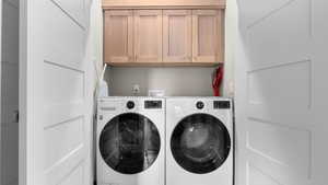 Clothes washing area featuring washer and clothes dryer and cabinets