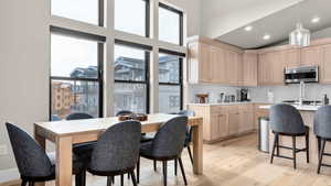 Kitchen featuring light brown cabinets, a towering ceiling, hanging light fixtures, and light hardwood / wood-style flooring