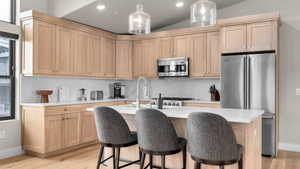 Kitchen with appliances with stainless steel finishes, light hardwood / wood-style flooring, vaulted ceiling, and light brown cabinetry