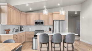 Kitchen with light brown cabinets, light hardwood / wood-style flooring, vaulted ceiling, and premium appliances