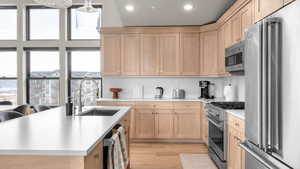 Kitchen featuring light brown cabinetry, premium appliances, a center island with sink, and a wealth of natural light