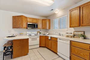 Kitchen featuring kitchen peninsula, a breakfast bar, white appliances, sink, and light tile patterned floors