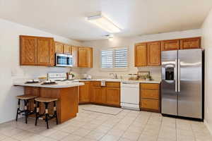 Kitchen with kitchen peninsula, appliances with stainless steel finishes, a breakfast bar, sink, and light tile patterned floors