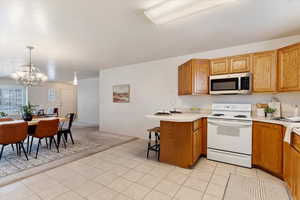 Kitchen with decorative light fixtures, light tile patterned floors, white range with electric stovetop, kitchen peninsula, and a chandelier