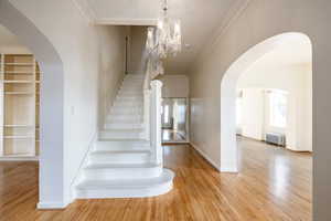 Stairs with hardwood / wood-style floors, radiator heating unit, crown molding, and a chandelier