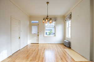 Unfurnished dining area with a chandelier, wood-type flooring, radiator, and ornamental molding