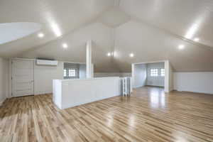 Additional living space featuring an AC wall unit, light hardwood / wood-style flooring, and vaulted ceiling