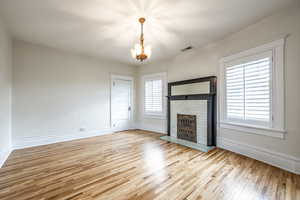 Unfurnished living room featuring a fireplace, light hardwood / wood-style floors, an inviting chandelier, and a wealth of natural light