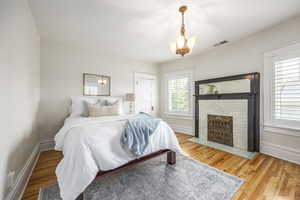 Bedroom featuring a brick fireplace, hardwood / wood-style floors, and an inviting chandelier