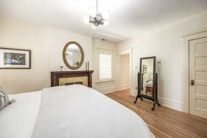 Bedroom featuring hardwood / wood-style floors, a brick fireplace, and a notable chandelier