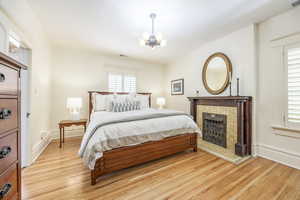 Bedroom with a chandelier, light hardwood / wood-style floors, and a brick fireplace