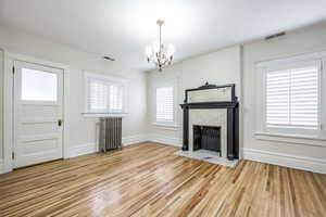 Unfurnished living room featuring a chandelier, radiator heating unit, a healthy amount of sunlight, and hardwood / wood-style floors