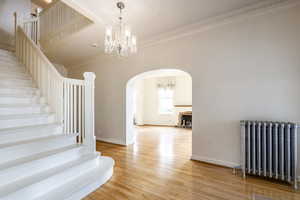 Stairs featuring hardwood / wood-style floors, an inviting chandelier, radiator, and crown molding