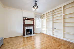 Unfurnished living room featuring wood-type flooring, crown molding, a high end fireplace, and an inviting chandelier