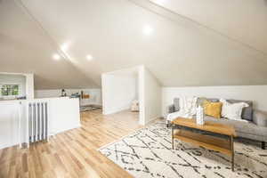 Additional living space with vaulted ceiling, radiator heating unit, and light hardwood / wood-style flooring