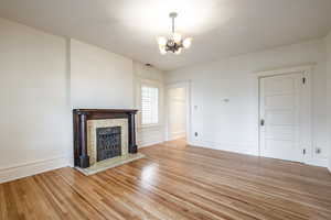 Unfurnished living room featuring a brick fireplace, light wood-type flooring, and an inviting chandelier