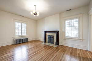 Unfurnished living room with radiator, light hardwood / wood-style floors, and an inviting chandelier