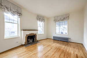 Unfurnished living room featuring radiator heating unit, a stone fireplace, and wood-type flooring