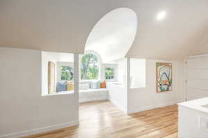 Hallway with light wood-type flooring and lofted ceiling