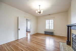 Unfurnished living room with a brick fireplace, an inviting chandelier, light hardwood / wood-style flooring, and radiator