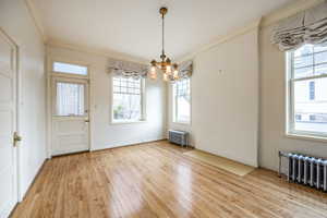 Unfurnished dining area with wood-type flooring, radiator, ornamental molding, and a notable chandelier