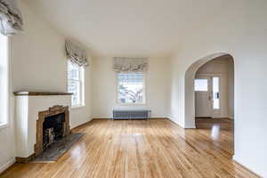 Unfurnished living room featuring a fireplace, radiator heating unit, and light wood-type flooring