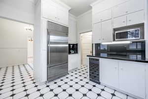 Kitchen featuring built in appliances, decorative backsplash, a notable chandelier, white cabinetry, and beverage cooler