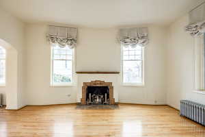 Unfurnished living room featuring light hardwood / wood-style floors, a healthy amount of sunlight, a fireplace, and radiator