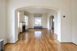 Unfurnished living room with light hardwood / wood-style flooring, a stone fireplace, and radiator