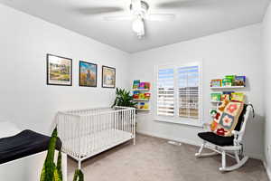 Carpeted bedroom with ceiling fan and a crib