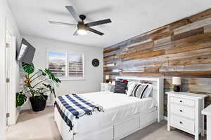 Bedroom with light carpet, ceiling fan, and wooden walls