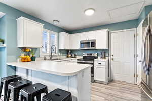 Kitchen featuring white cabinetry, sink, stainless steel appliances, kitchen peninsula, and a breakfast bar area