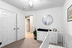 Carpeted bedroom with a crib, a textured ceiling, a closet, and ceiling fan