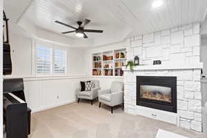 Living area featuring ceiling fan, wooden ceiling, a stone fireplace, a tray ceiling, and light carpet