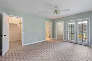 Interior space featuring light carpet, french doors, a walk in closet, ceiling fan, and a closet