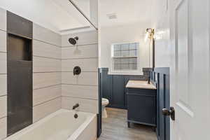 Full bathroom with wood-type flooring, vanity, toilet, and tiled shower / bath combo