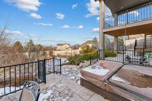 Snow covered patio featuring a balcony and a hot tub