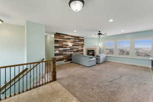 Living room with wooden walls, a fireplace, light tile patterned floors, and ceiling fan