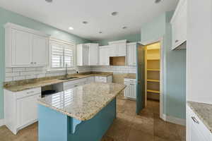 Kitchen featuring white cabinetry, a center island, light stone countertops, sink, and tasteful backsplash