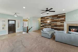 Unfurnished living room featuring ceiling fan, light colored carpet, wooden walls, and a tiled fireplace