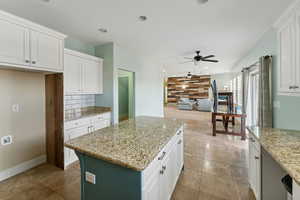 Kitchen with light stone countertops, a center island, white cabinetry, and ceiling fan