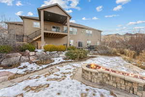 Snow covered house featuring a mountain view, a balcony, a fire pit, and a patio area