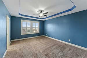 Empty room featuring ceiling fan, carpet floors, and a tray ceiling