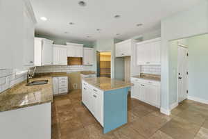 Kitchen with stone countertops, a kitchen island, white cabinetry, and sink