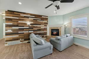 Living room featuring carpet flooring, ceiling fan, wood walls, and a fireplace